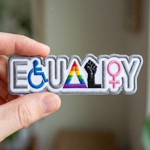 May include: Embroidered patch with the word "EQUALITY" in a gray, outlined font. The design includes a blue wheelchair symbol, a rainbow triangle, a black raised fist, and a pink female symbol.