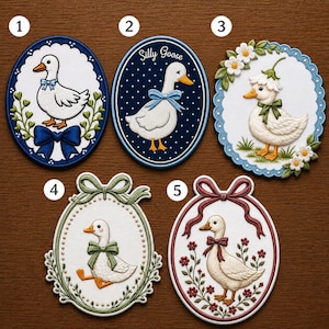 May include: A collection of five embroidered patches featuring charming goose designs. Each patch showcases a white goose with a bow, set within oval frames with floral or decorative borders. The patches vary in color, including blue, green, and red accents.