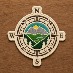 May include: A circular embroidered patch featuring a compass design with cardinal directions N, S, E, and W. The center depicts a landscape with grey mountains, a yellow sun, a winding blue river, and dark green pine trees against a teal sky.