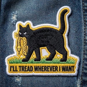 May include: Embroidered patch featuring a black cat carrying a yellow snake in its mouth, set against a green and yellow grass design. The patch has the text "I'LL TREAD WHEREVER I WANT" in white letters.