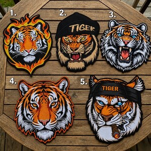 May include: Five embroidered tiger patches. Patch 1 shows a tiger head surrounded by orange flames. Patch 2 features a tiger wearing a black cap with the text TIGER. Patch 3 depicts a snarling tiger. Patch 4 shows a tiger face. Patch 5 features a tiger wearing a headband with the text TIGER and smoking a cigar.
