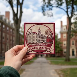 May include: A square patch featuring a detailed illustration of Harvard University buildings, with the text "MASSACHUSETTS HARVARD UNIVERSITY" in a banner. The patch has a maroon border and a beige background, showcasing the university's architecture.
