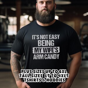 Bearded man wearing black "Wife's Arm Candy" shirt, with text saying that we carry Shirts and Hoodies in Big sizes 3XL to 6XL and Tall sizes LT, XLT, 2XLT, 3XLT, and 4XLT
