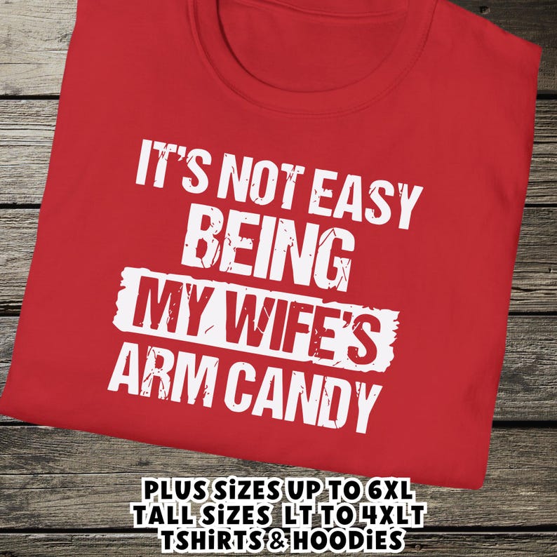 Funny Gift for Husband - a tshirt with text saying "It's not easy being my wife's arm candy" on a Red shirt - image includes a text overlay saying that we carry Shirts and Hoodies in Big sizes 3XL, 4XL, 5XL, and 6XL and Tall sizes LT, XLT, 2XLT, 3XLT, and 4XLT