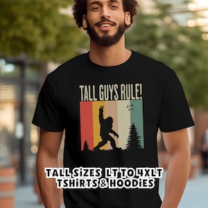 Puede incluir: Camiseta negra con el texto "TALL GUYS RULE!" y un gr&aacute;fico de silueta de Bigfoot. El gr&aacute;fico utiliza una combinaci&oacute;n de colores retro con rayas verticales. La camiseta tambi&eacute;n dice "TALL SIZES LT TO 4XLT TSHIRTS & HOODIES".