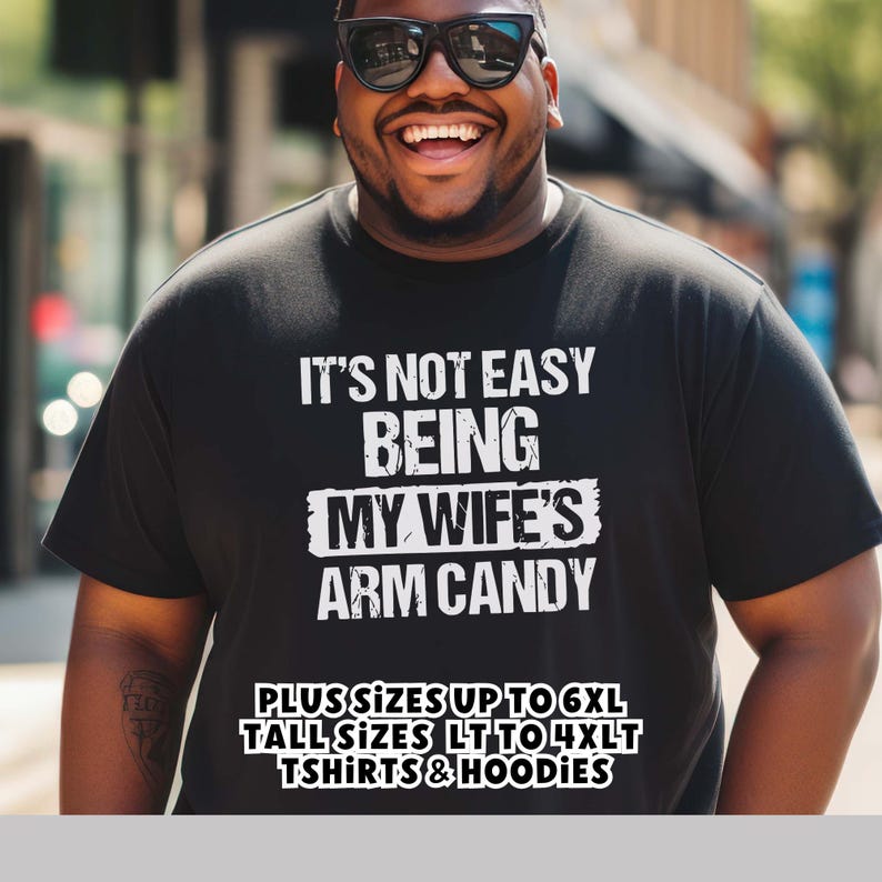 Funny Gift for Husband - a Black Tshirt with text saying "It's not easy being my wife's arm candy" - image includes a text overlay saying that we carry TShirts and Hoodies in Big sizes 3XL, 4XL, 5XL, and 6XL and Tall sizes LT, XLT, 2XLT, 3XLT, and 4XLT