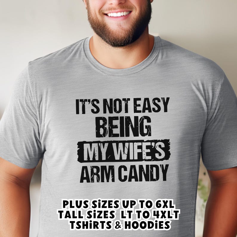 Funny Gift for Husband - a young man wearing a sport grey Tshirt with text saying "It's not easy being my wife's arm candy" - image includes a text overlay saying that we carry TShirts and Hoodies in Big sizes 3XL, 4XL, 5XL, and 6XL and Tall sizes LT, XLT, 2XLT, 3XLT, and 4XLT