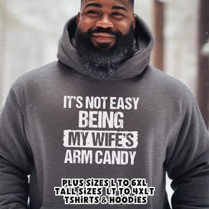 Funny Gift for Husband - a pullover hoodie sweatshirt with text saying "It's not easy being my wife's arm candy" - image includes a text overlay saying that we carry TShirts and Hoodies in Big sizes 3XL, 4XL, 5XL, and 6XL and Tall sizes LT, XLT, 2XLT, 3XLT, and 4XLT