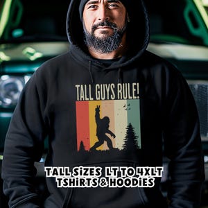 Puede incluir: Sudadera con capucha negra con el texto "TALL GUYS RULE!" y una silueta de Bigfoot. El dise&ntilde;o incluye rayas verticales en rojo, naranja, amarillo y verde. Tambi&eacute;n se ve el texto "TALL SIZES LT TO 4XLT TSHIRTS & HOODIES".