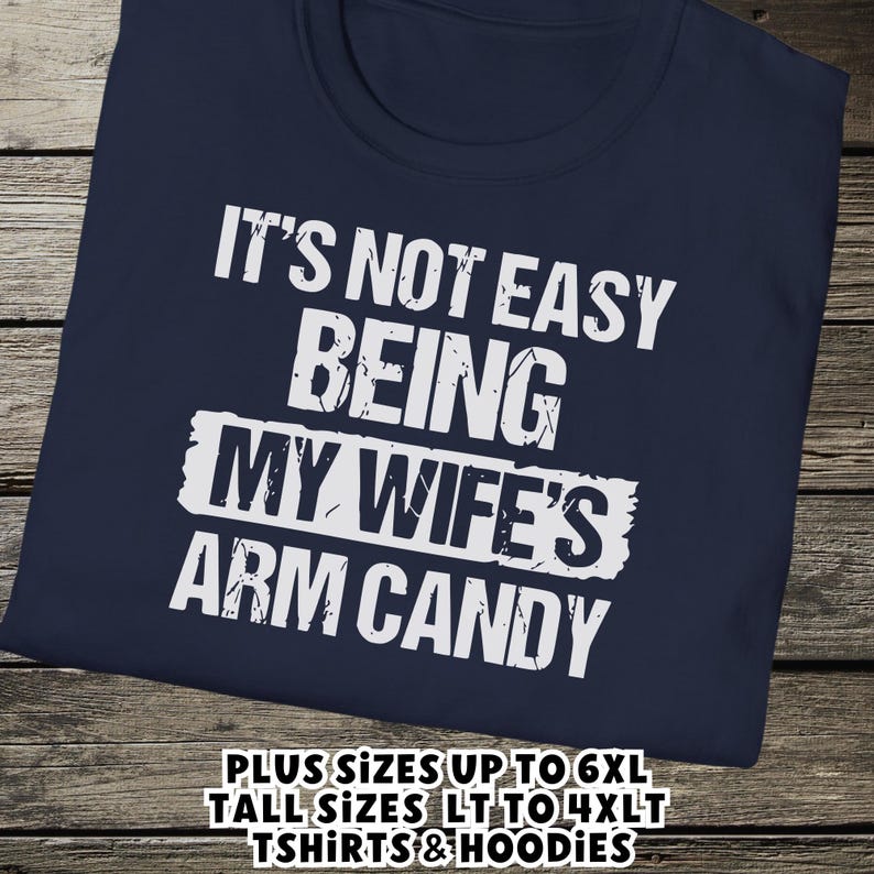 Funny Gift for Husband - a tshirt with text saying "It's not easy being my wife's arm candy" on a Navy Blue shirt - image includes a text overlay saying that we carry Shirts and Hoodies in Big sizes 3XL, 4XL, 5XL, and 6XL and Tall sizes LT, XLT, 2XLT, 3XLT, and 4XLT