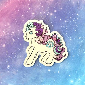 May include: A sticker featuring a cartoon pony with a cream-colored body, blue eyes, and a flowing mane and tail in shades of purple, pink, and blue. The pony has a pink bow and blue floral accents. The background is a gradient of blue, purple, and pink.