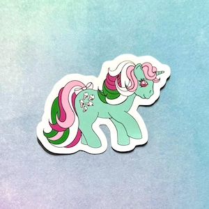May include: A sticker featuring a cartoon pony with a light green body, pink and green mane and tail, and a single horn. The pony has a pink bow and ice cream cone details on its tail. The background is a gradient of blue and purple.
