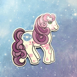 May include: A sticker of a white pony with a purple mane and tail. The pony has pink floral and heart designs on its body. The background is a light blue with white stars.