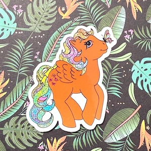 May include: Orange pony sticker with a rainbow mane, tail, and wings. A butterfly rests on its nose. The sticker has a white border and is set against a dark background with a tropical leaf pattern.