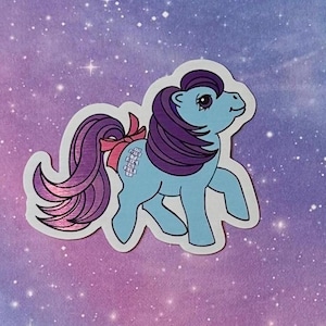 May include: A blue and purple pony with a pink bow and a rainbow-colored mane. The pony is standing on a white background with a galaxy pattern.