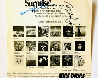 May include: A cream-coloured promotional paper insert featuring the text Surprise! and Nice Price. It displays a grid of 15 small black and white album cover images with artist names and titles. Two distinct black ink signatures are visible on the surface.