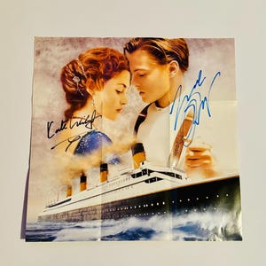 May include: A vintage movie poster featuring a black and white image of the Titanic with a couple in the foreground. The poster is signed by Kate Winslet and Leonardo DiCaprio.