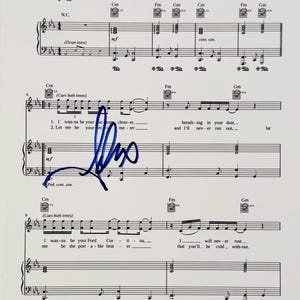 May include: A sheet music page featuring black musical notation on a white background with a prominent blue ink signature overlaid across the centre. The lyrics include lines such as I wanna be your vacuum cleaner and I wanna be your Ford Cortina.