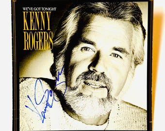 Könnte beinhalten: Ein quadratisches Schallplattencover mit einem sepiafarbenen Porträt von Kenny Rogers. Der Text lautet WE'VE GOT TONIGHT und KENNY ROGERS in Gelb. Eine blaue Tintensignatur ist im unteren linken Bereich des Gesichts und des Pullovers zu sehen.