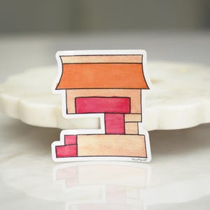 May include: A die-cut sticker featuring a stylized, geometric illustration of a building with a peach-colored roof, a central rectangular section in deep pink, and a lower level with pink accents, all outlined in a thin black line.