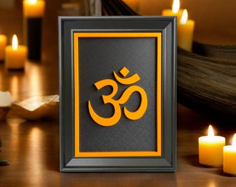 May include: Framed artwork featuring the Om symbol in bright orange against a textured black background. The frame is dark gray with an orange inner border. Lit candles in the background create a warm, inviting ambiance.