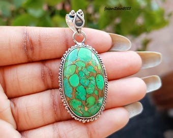 May include: A silver pendant with a green and gold oval turquoise stone. The stone has a unique pattern of green and gold.