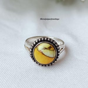 May include: A silver ring with a large, round, yellow and white stone. The stone is set in a beaded bezel. The ring is on a white surface. The text "Shreejaipurjewels92" is in the upper right corner.