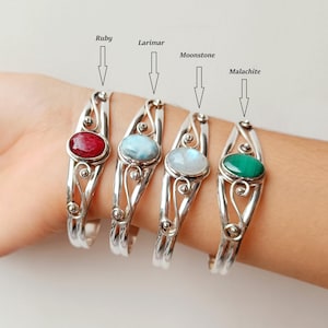 Pode incluir: Quatro pulseiras de prata com pedras preciosas ovais: rubi, larimar, pedra da lua e malaquite. Cada pulseira apresenta um design decorativo vazado. As pedras são engastadas em uma moldura.