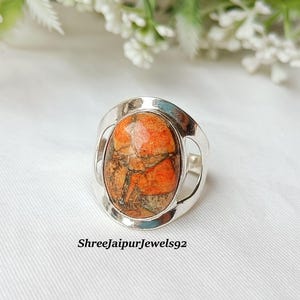 May include: A silver ring with an oval-shaped, orange and brown stone. The stone has a textured appearance. The ring's band is a simple, open design. The text "Shreejaipurjewels92" is at the bottom of the image.