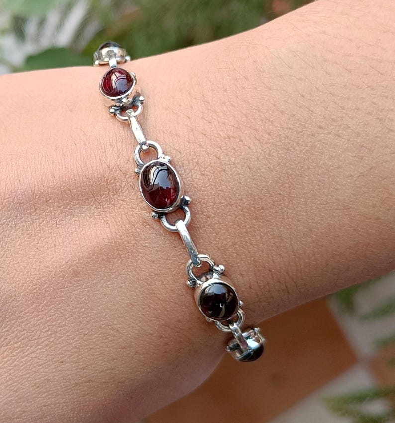 May include: A silver bracelet with five oval-shaped red gemstones. The bracelet is on a person's wrist.
