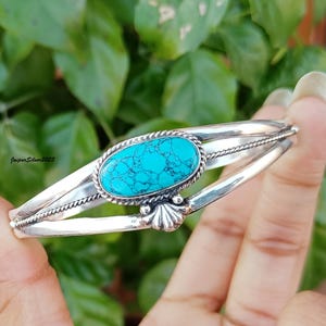 May include: A silver bangle bracelet with a turquoise stone set in a silver oval. The bracelet has a twisted wire design.