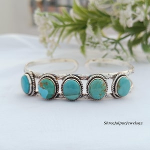 May include: A silver cuff bracelet featuring five oval-shaped turquoise stones set in twisted wire bezels. The metal band has an engraved floral pattern and an open back design. The text ShreeJaipurJewels92 is visible in the bottom right corner.