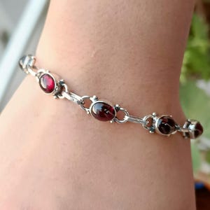 May include: A silver chain bracelet with red gemstone accents. The bracelet features oval-shaped gemstones set in silver.