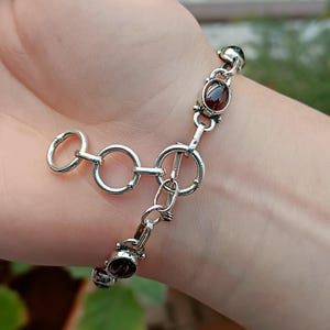 May include: A silver bracelet with a clasp closure and oval-shaped red gemstones.