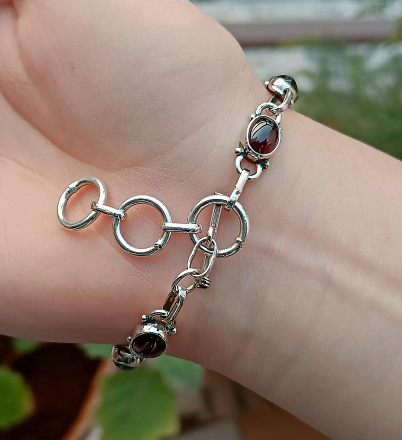 May include: A silver bracelet with a clasp closure and oval-shaped red gemstones.