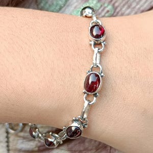 May include: A silver bracelet with red gemstone accents. The bracelet has a chain link design with oval-shaped gemstones.