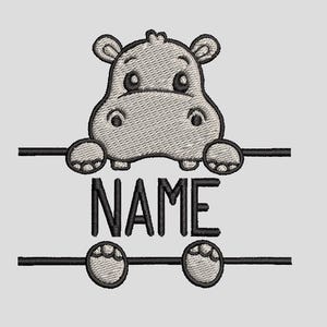 May include: An embroidered design featuring a cartoon hippo with the word "NAME" in bold, black letters. The hippo is light gray with black outlines and details. The design includes horizontal black lines with the hippo's paws and feet.