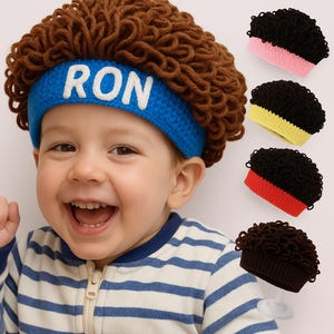 May include: A child wearing a brown curly wig with a blue headband that says "RON" in white letters. Several small black curly wigs with different colored bands are displayed to the right.