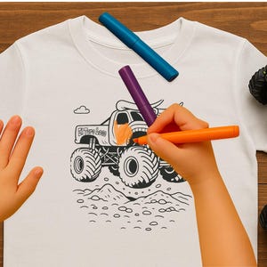 May include: A white t-shirt with a black monster truck graphic is being colored with orange and purple markers. The text "El Toro Loco" is visible on the truck. Toy monster trucks and markers are scattered around the shirt.