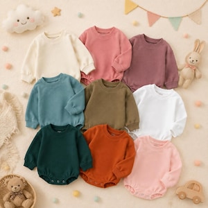 Könnte beinhalten: Eine Kollektion von acht langärmeligen Baby-Bodys in verschiedenen Unifarben wie Creme, Altrosa, Mauve, Petrol, Olivgrün, Weiß, Dunkelgrün und Rostorange, jeweils mit Rundhalsausschnitt und Druckknöpfen im Schrittbereich versehen.