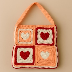 May include: A handmade crochet bag featuring a patchwork design with four squares. Each square has a heart in the center. The bag is peach, red, and white with a matching peach strap.