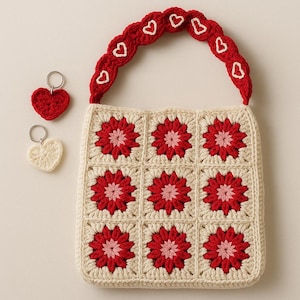 Peut inclure: Un sac fourre-tout en crochet crème avec des carrés de fleurs rouges et une poignée rouge ornée de cœurs blancs. Deux porte-clés en forme de cœur, un rouge et un crème, sont également présents. Le sac est fait à la main.