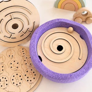 Puede incluir: Juguetes de madera que incluyen un laberinto, un juego en espiral con una bola y un juego de emparejamiento de números. También hay un arcoíris de madera y un pequeño coche de madera. El juego en espiral tiene un borde de fieltro morado. El juego de números tiene el nombre "RICCARDO".