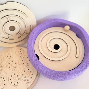 Può includere: Giocattoli di labirinto e puzzle numerici in legno. Un labirinto è rotondo con un design a spirale e una pallina. Un altro è un labirinto rotondo con un percorso complesso. Un terzo puzzle presenta palloncini con i numeri 1-9.