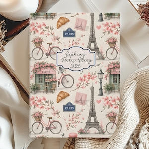 May include: A journal with a Parisian theme. The cover features illustrations of bicycles, the Eiffel Tower, croissants, and floral accents. The text "Sophia's Paris Story 2026" is displayed on the cover.