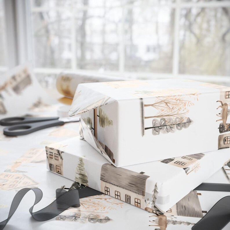 May include: Two rectangular gift boxes wrapped in white paper with a repeating pattern of houses, trees, and deer in muted brown and green tones. Black scissors and a roll of black ribbon are also visible.