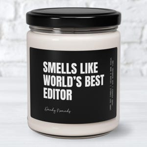 May include: A white candle with a black label that reads "Smells Like World's Best Editor" and "Dandy Nomads".