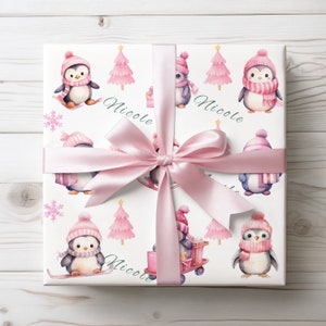 May include: A wrapped gift with a white background featuring a repeating pattern of penguins in pink hats and scarves, pink Christmas trees, and snowflakes. The gift is tied with a pink satin ribbon and bow. The name "Nicole" is written in green cursive.