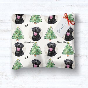 Pode incluir: Papel de embrulho branco com um padr&atilde;o repetido de Labradores pretos, &aacute;rvores de Natal verdes e pegadas. A etiqueta de presente amarrada com uma fita vermelha diz "Charlie".