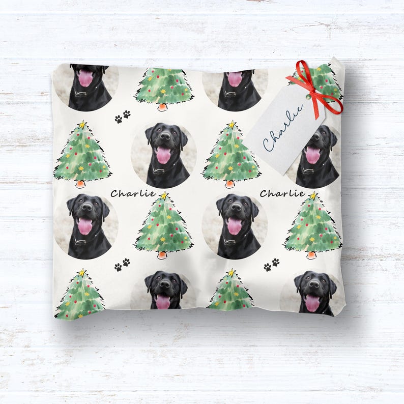 Pode incluir: Papel de embrulho branco com um padr&atilde;o repetido de Labradores pretos, &aacute;rvores de Natal verdes e pegadas. A etiqueta de presente amarrada com uma fita vermelha diz "Charlie".